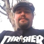 Author Mike Hilbig. He's in a black t-shirt that says THRASHER on the front and he has light skin, a short beard, and a flat cap.